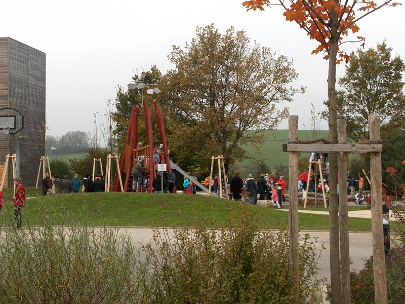 Auf dem Bild ist der Spielplatz der Schule zu sehen. Es sind Kinder und Erwachsene auf dem Platz.