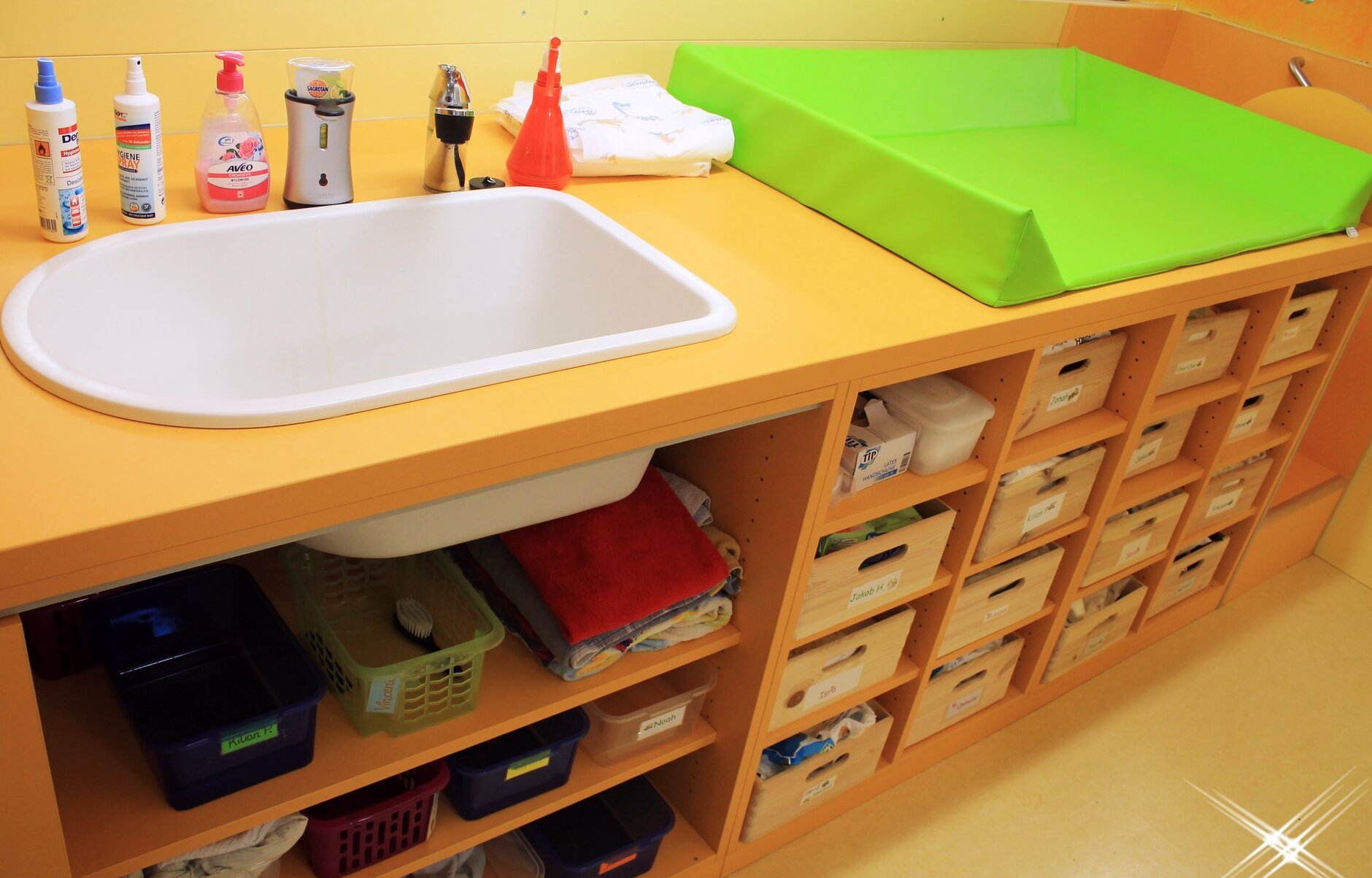 Auf dem Bild ist ein Wickeltisch mit Wickelablage, Waschbecken und Zubehör.