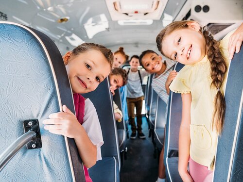 group of cute schoolchildren riding on school bus and looking at