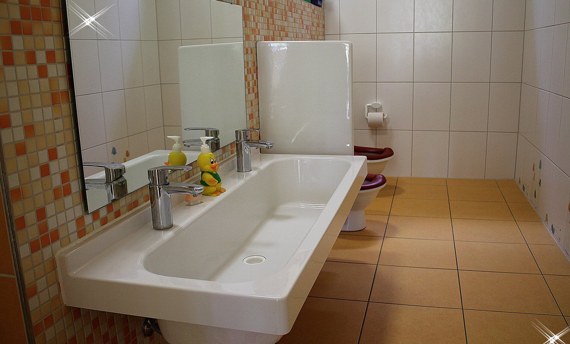 Auf dem Bild ist ein langes, niedriges Waschbecken in einem Waschraum zu sehen.